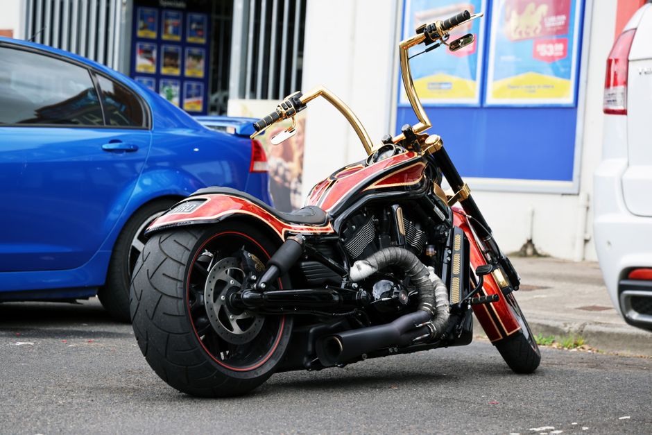 Vivid image of a custom motorcycle with golden handlebars parked between two cars on a city street.