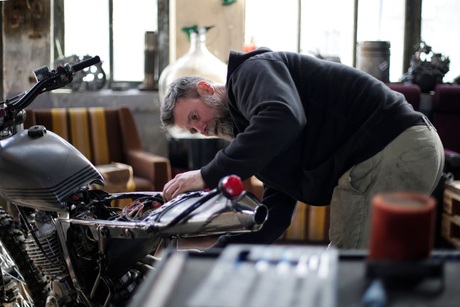Concentrated adult bearded male mechanic in workwear fixing electric details of motorbike while working alone in spacious light garage