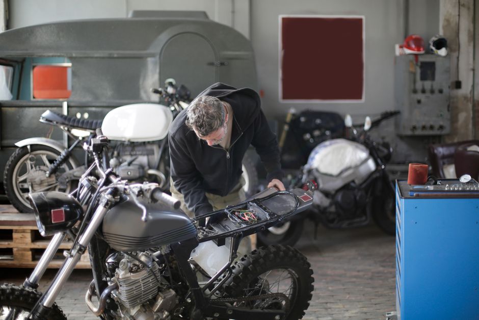 Middle aged bearded male mechanic in workwear and repairing motorbike while standing in modern spacious garage